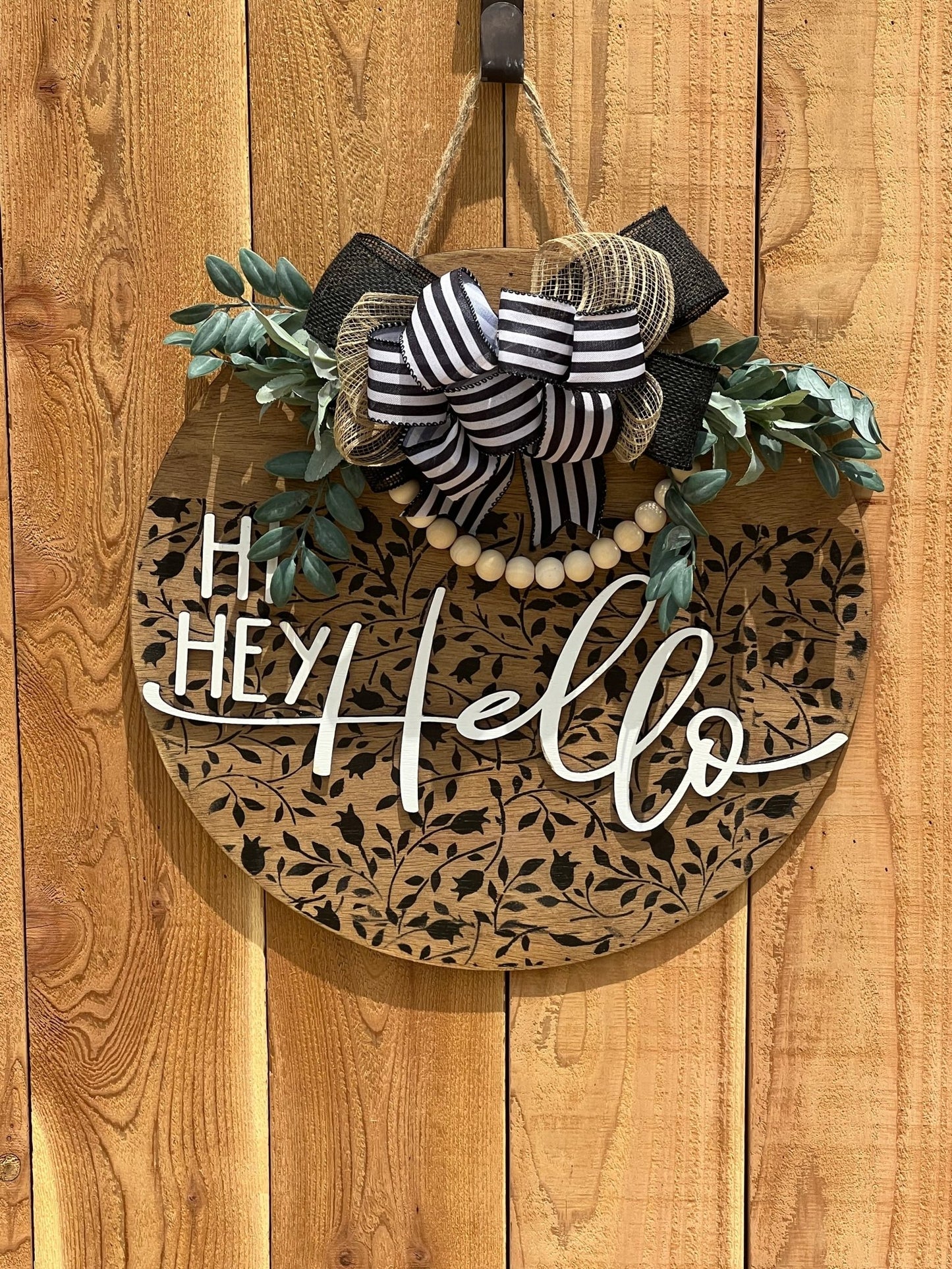 Round wood black Mini Flower and Vine door sign with natural wood accents hanging on an unpainted fence.