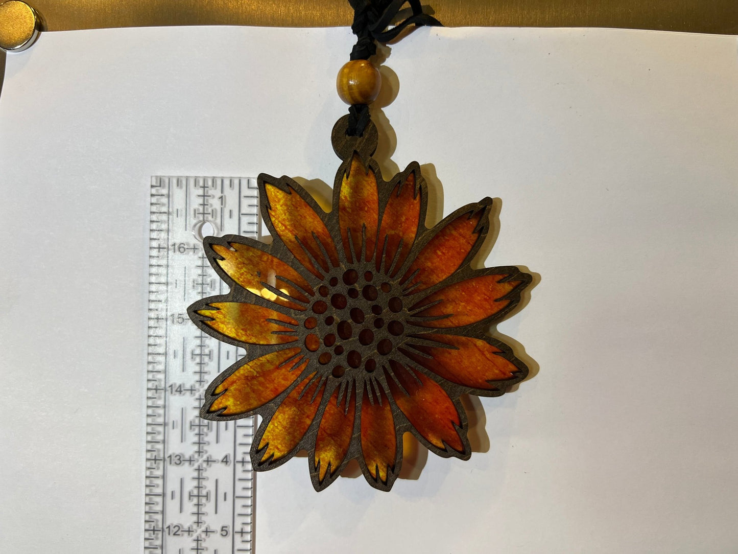 Sunflower suncatcher made of walnut stained wood and yellow acrylic, 4.5 inches in size, against white background with ruler.