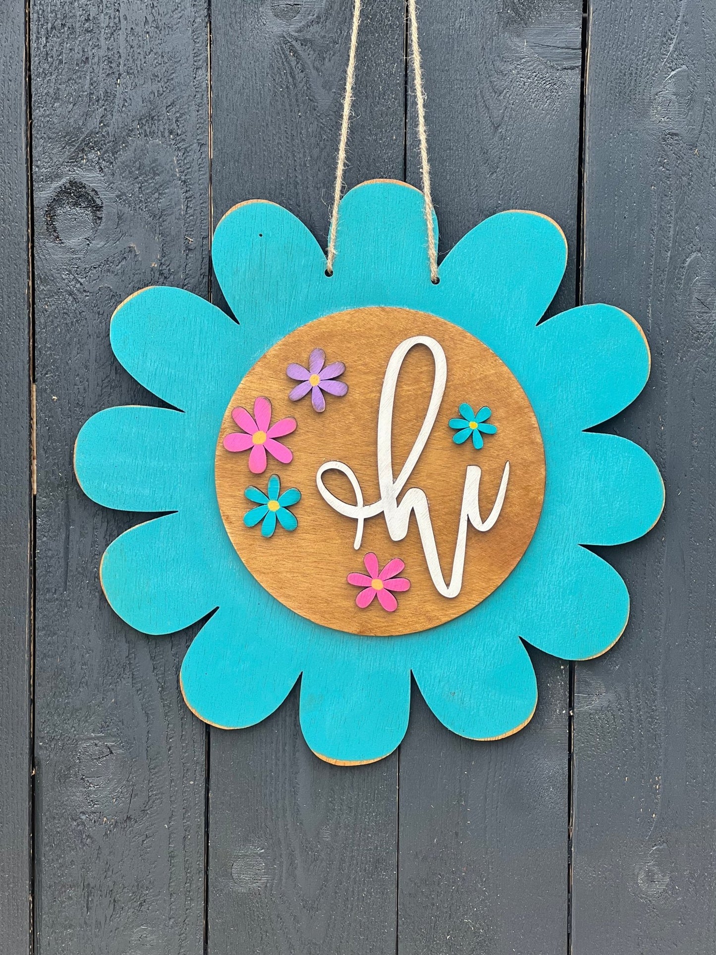 Turquoise flower door hanger made of natural wood with vibrant multicolor design on black fence.