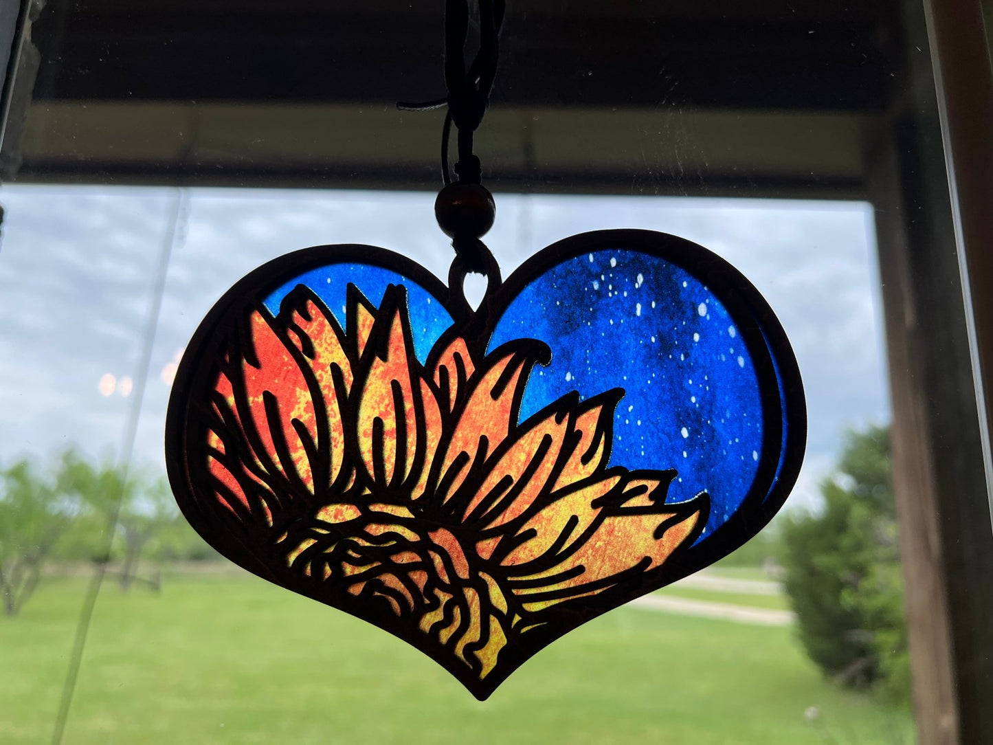 Heart-shaped suncatcher with sunflower design made of wood and multicolor acrylic, creating a stained glass effect in sunlight.