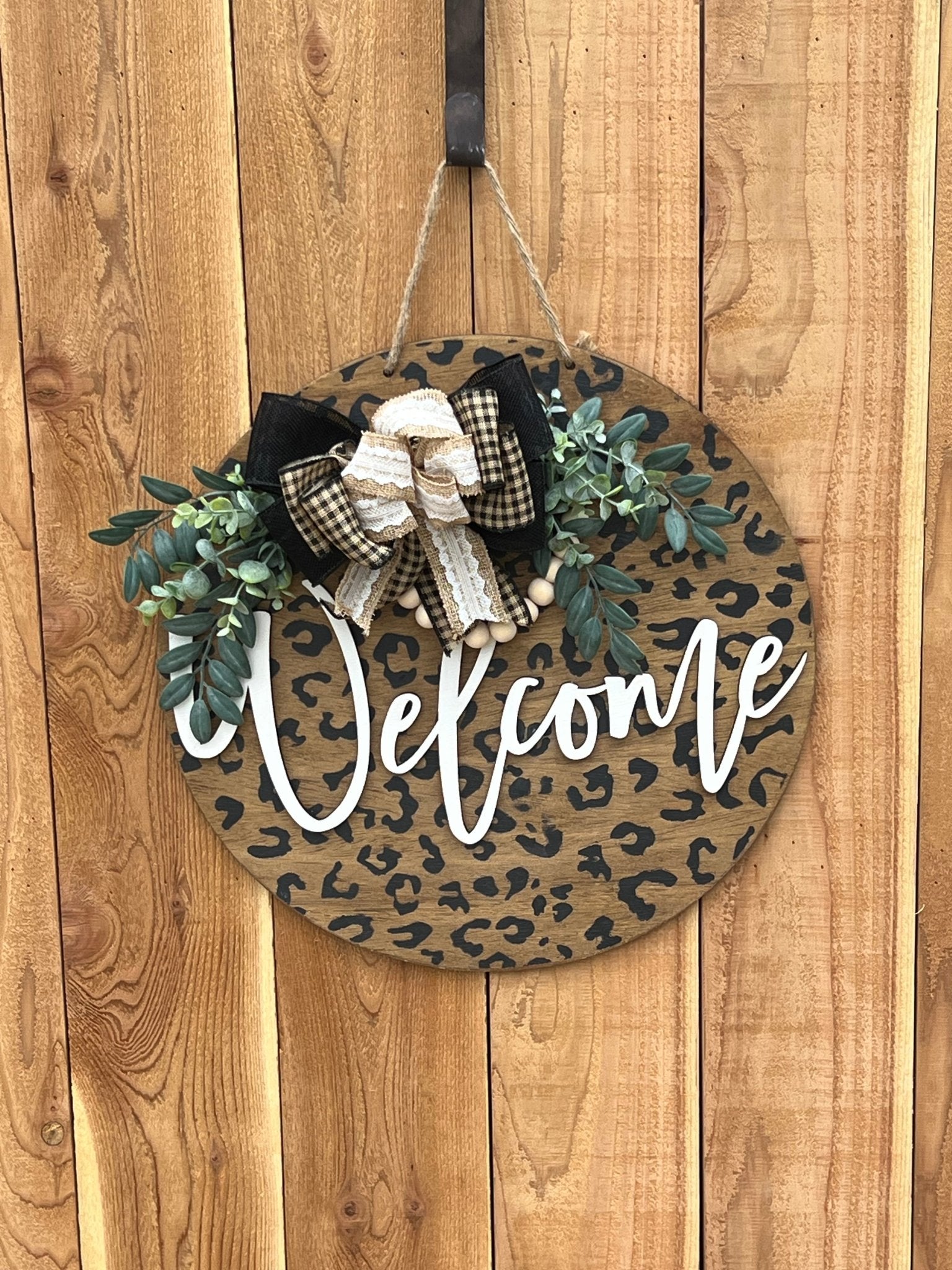 A rustic wooden door hanger with leopard print design, perfect for chic decor hanging on an unpainted fence.