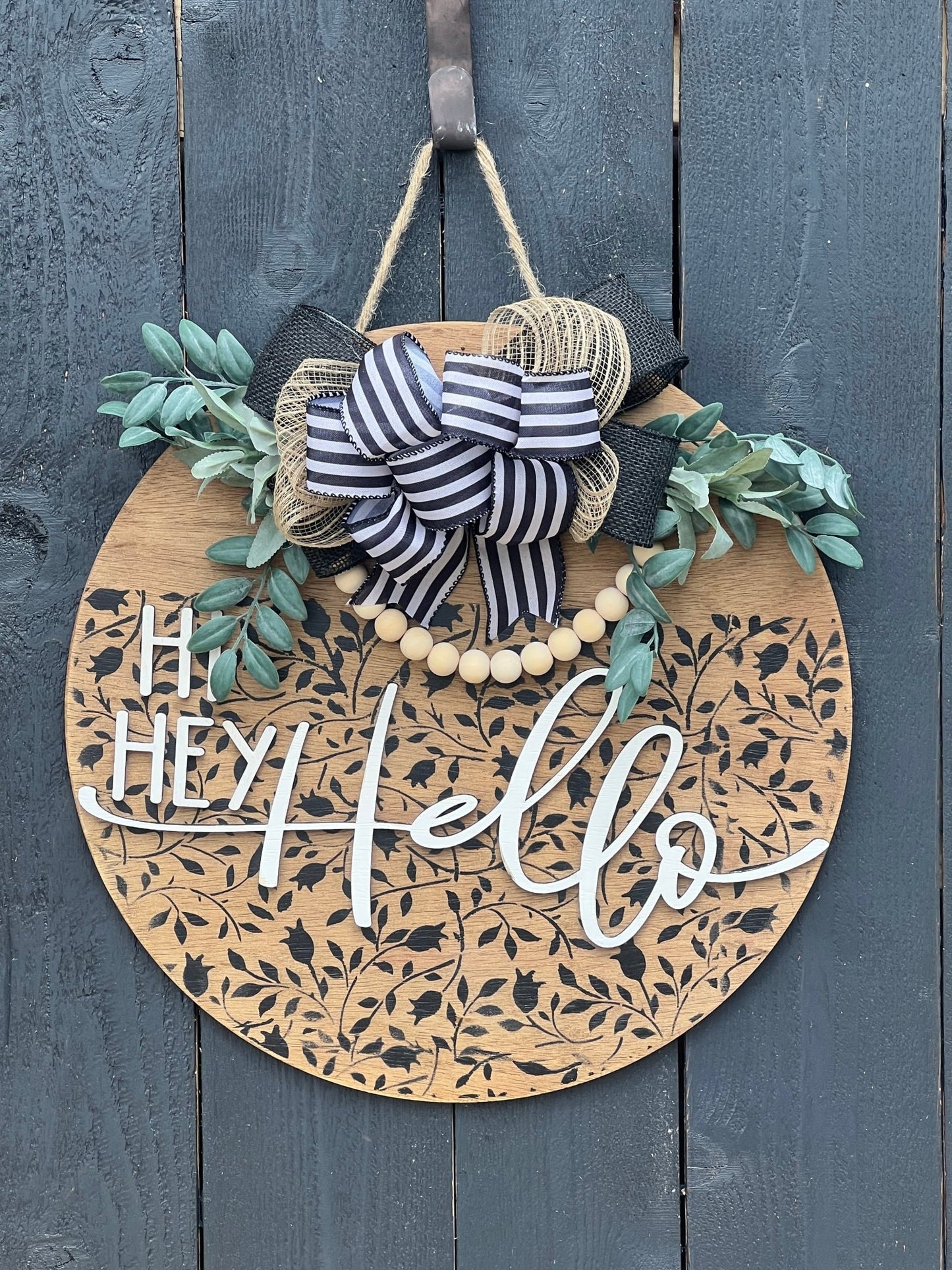 Round wood black Mini Flower and Vine door sign with natural wood accents hanging on a black fence.