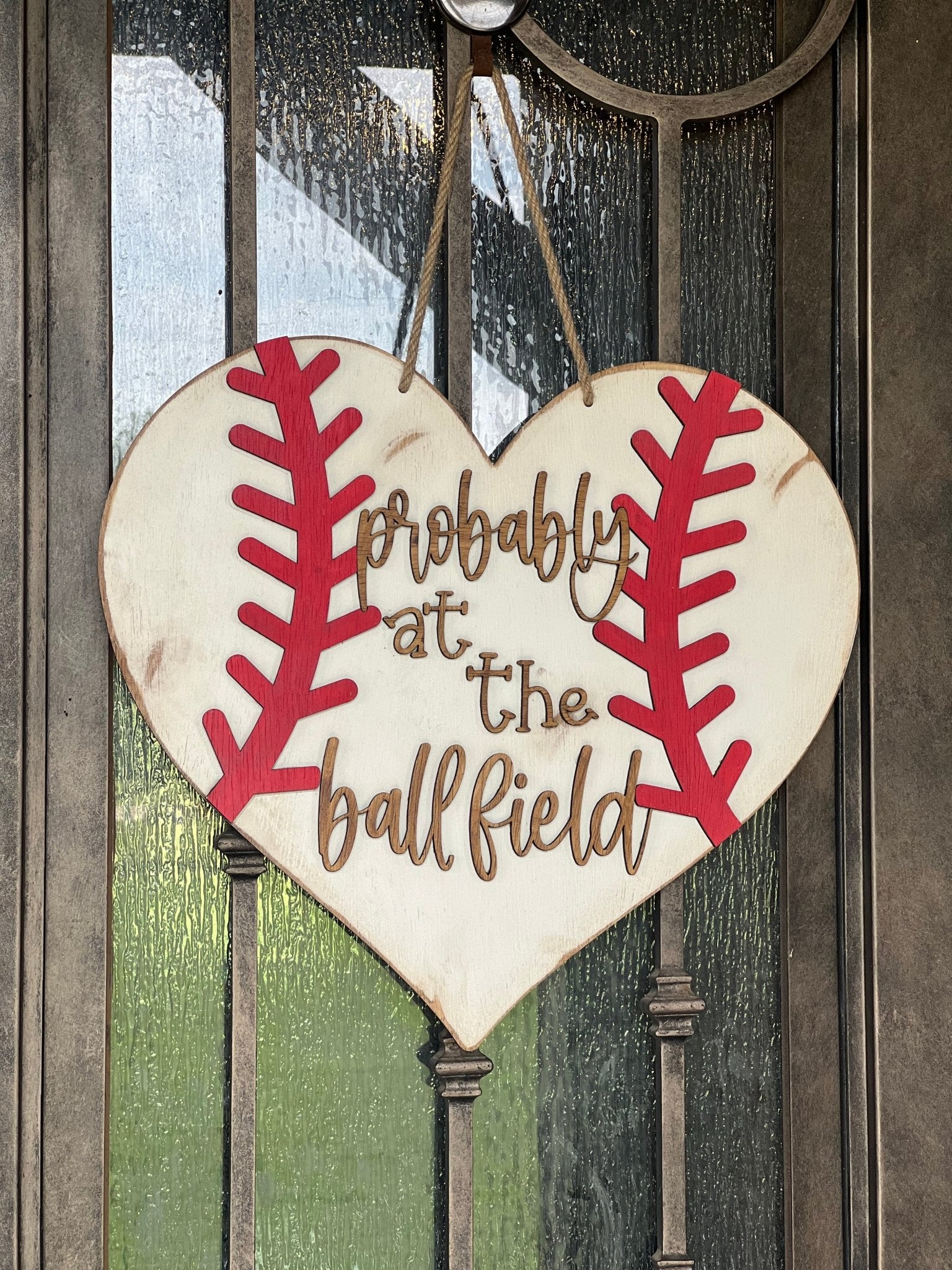 A rustic wooden door hanger shaped like a heart with baseball stitching in white and red on metal door.