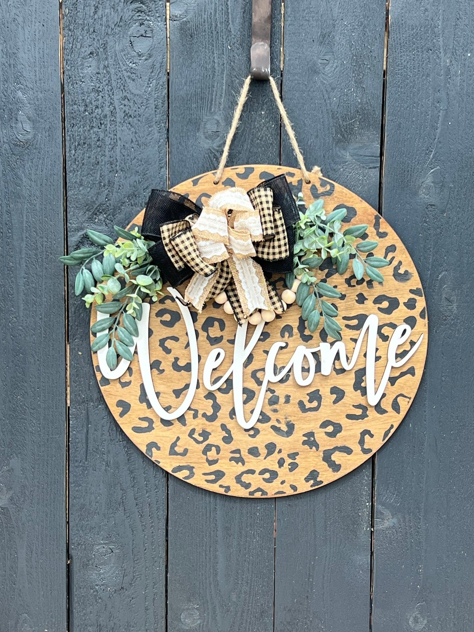 A rustic wooden door hanger with leopard print design, perfect for chic decor hanging on a black fence.