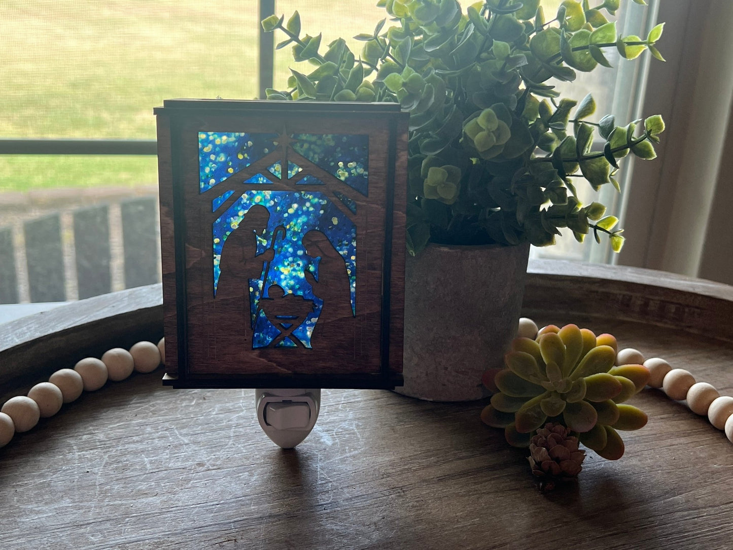 A Christmas Nativity Lantern Nightlight in golden oak with wood and acrylic materials  with natural light shining through.