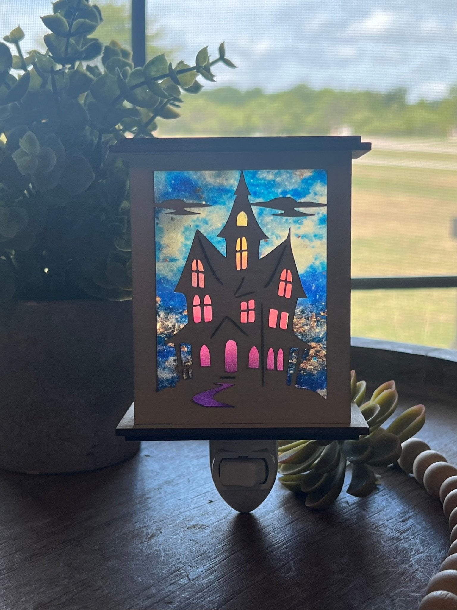 Halloween Haunted House Lantern Nightlight made from wood and acrylic, showcasing rustic charm and multicolor glow with sunlight filterring through.