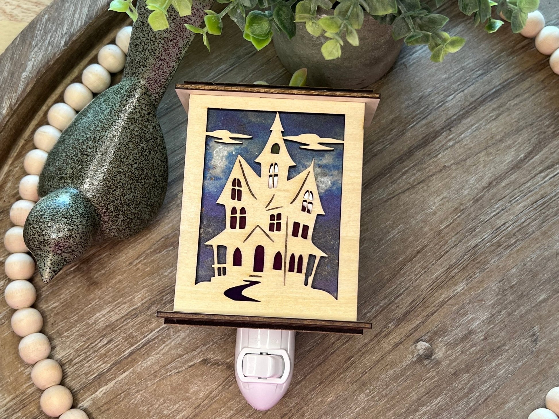 Halloween Haunted House Lantern Nightlight made from wood and acrylic, showcasing rustic charm and multicolor glow lying on a tray.