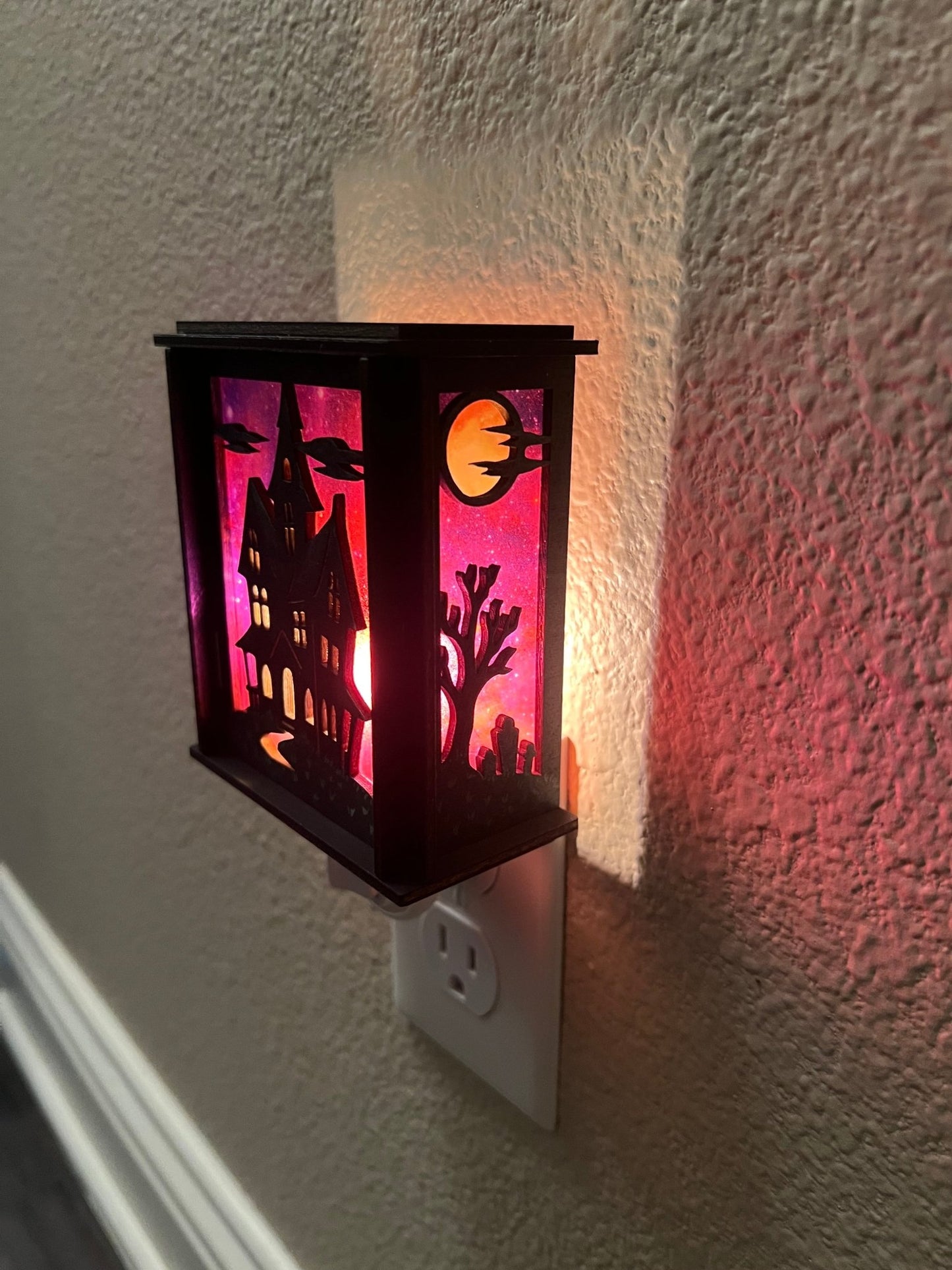 A lit right side view of a haunted house hand painted stained glass effect nightlight, multicolor acrylic and black wood design.