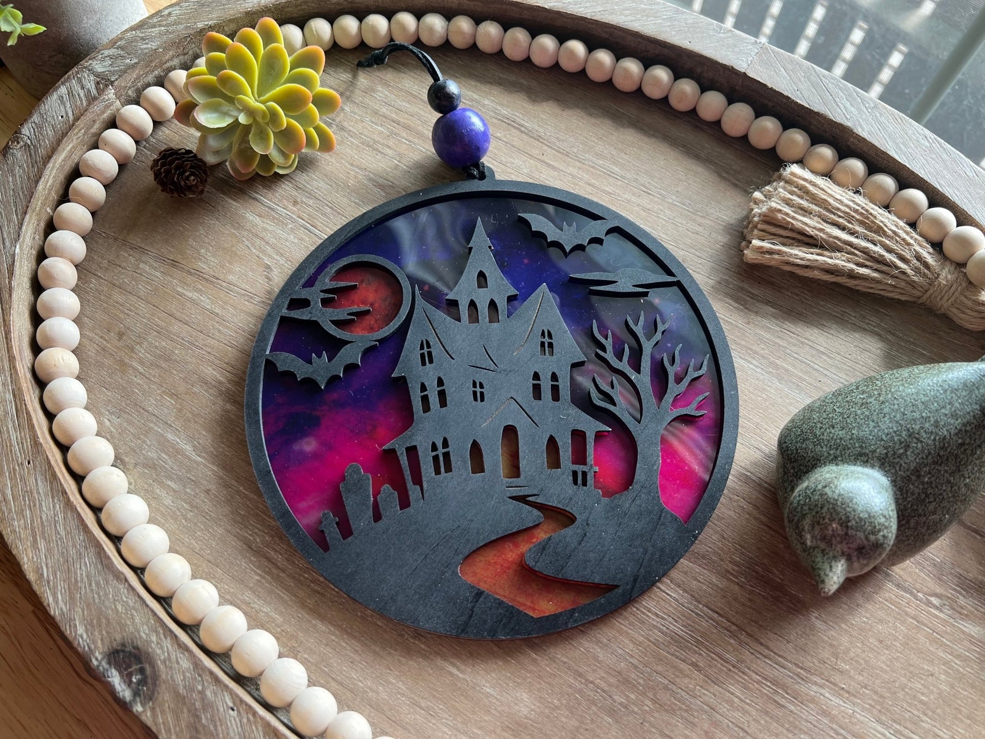Hand painted suncatcher with a haunted house design on wood and acrylic, in vibrant colors back view on tray.