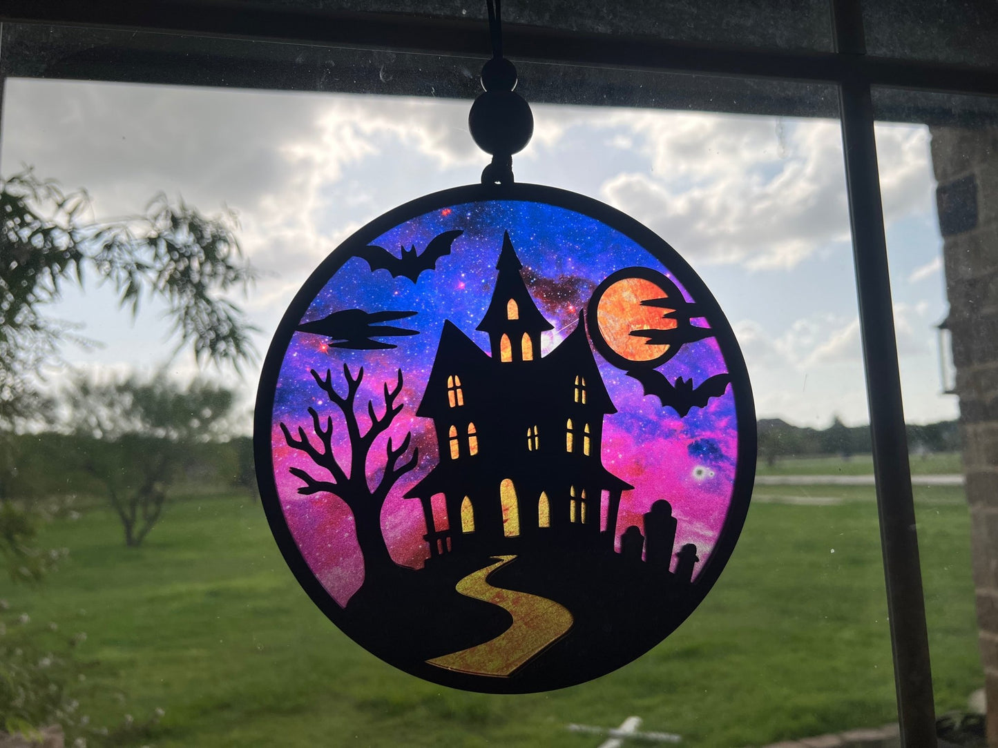 Hand painted suncatcher with a haunted house design on wood and acrylic, in vibrant colors - in sunlight.