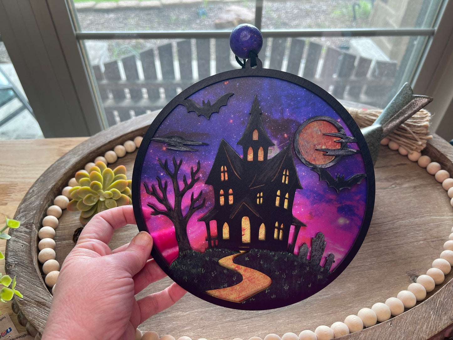 Hand painted suncatcher with a haunted house design on wood and acrylic, in vibrant colors in hand.