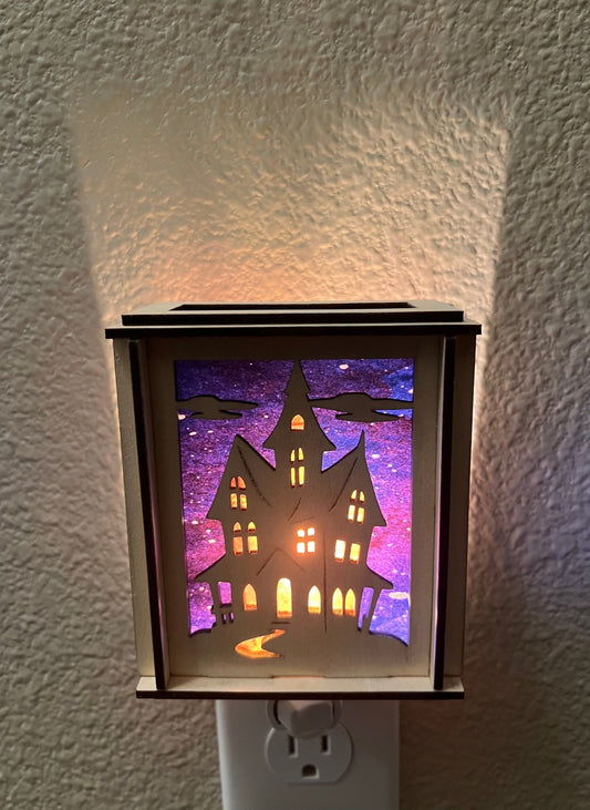 A haunted house-themed suncatcher with stained glass effect in black and multicolor acrylic - lighted from front.