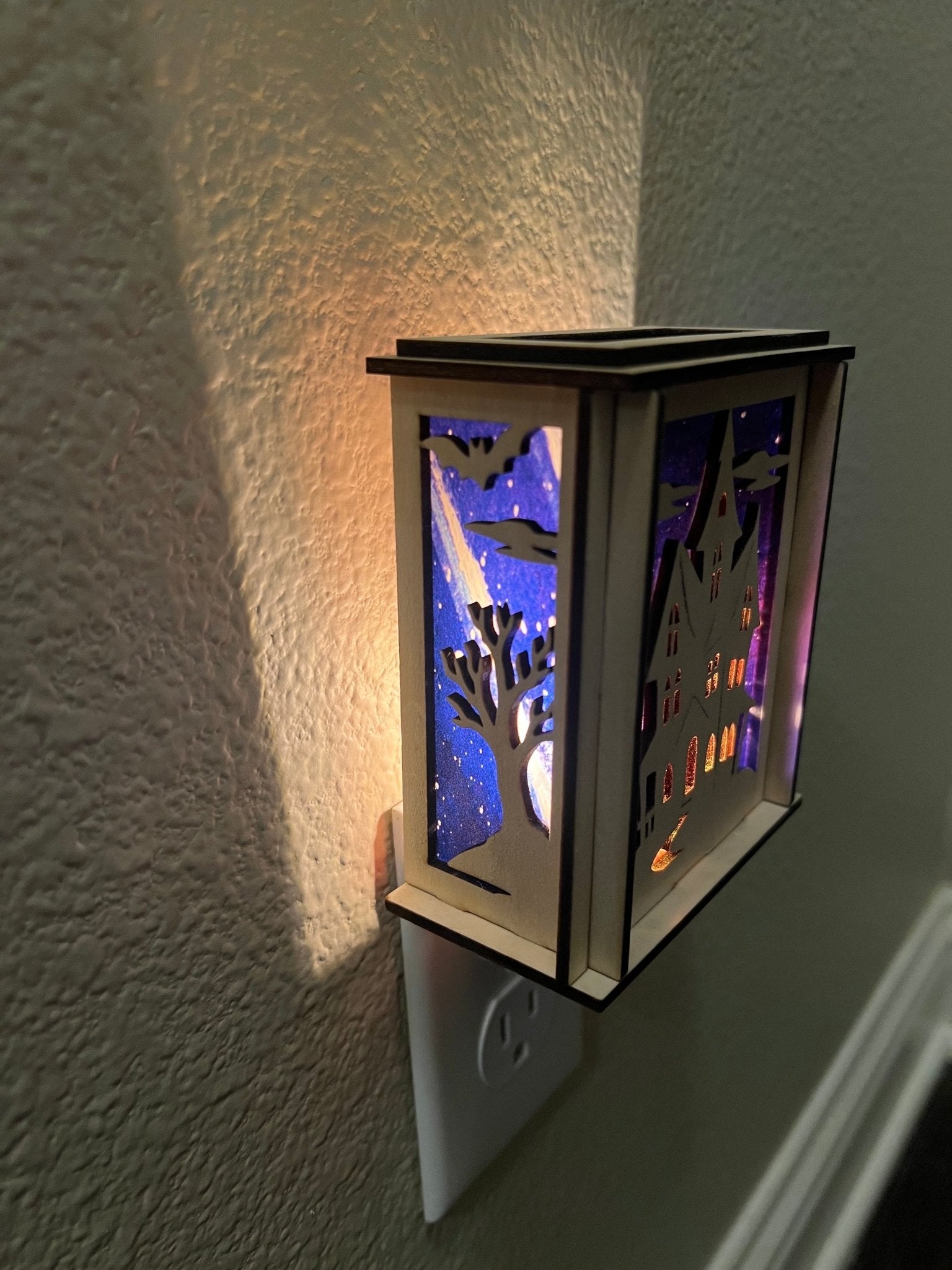 A haunted house-themed suncatcher with stained glass effect in black and multicolor acrylic - lighted form left side.