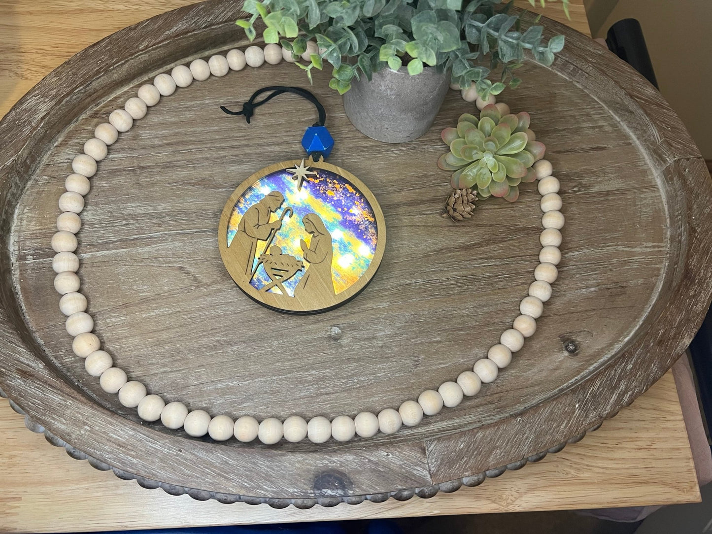 Lighted Christmas Nativity Ornament made of wood and acrylic, featuring a rustic, multicolor design lighted lying on a tray.