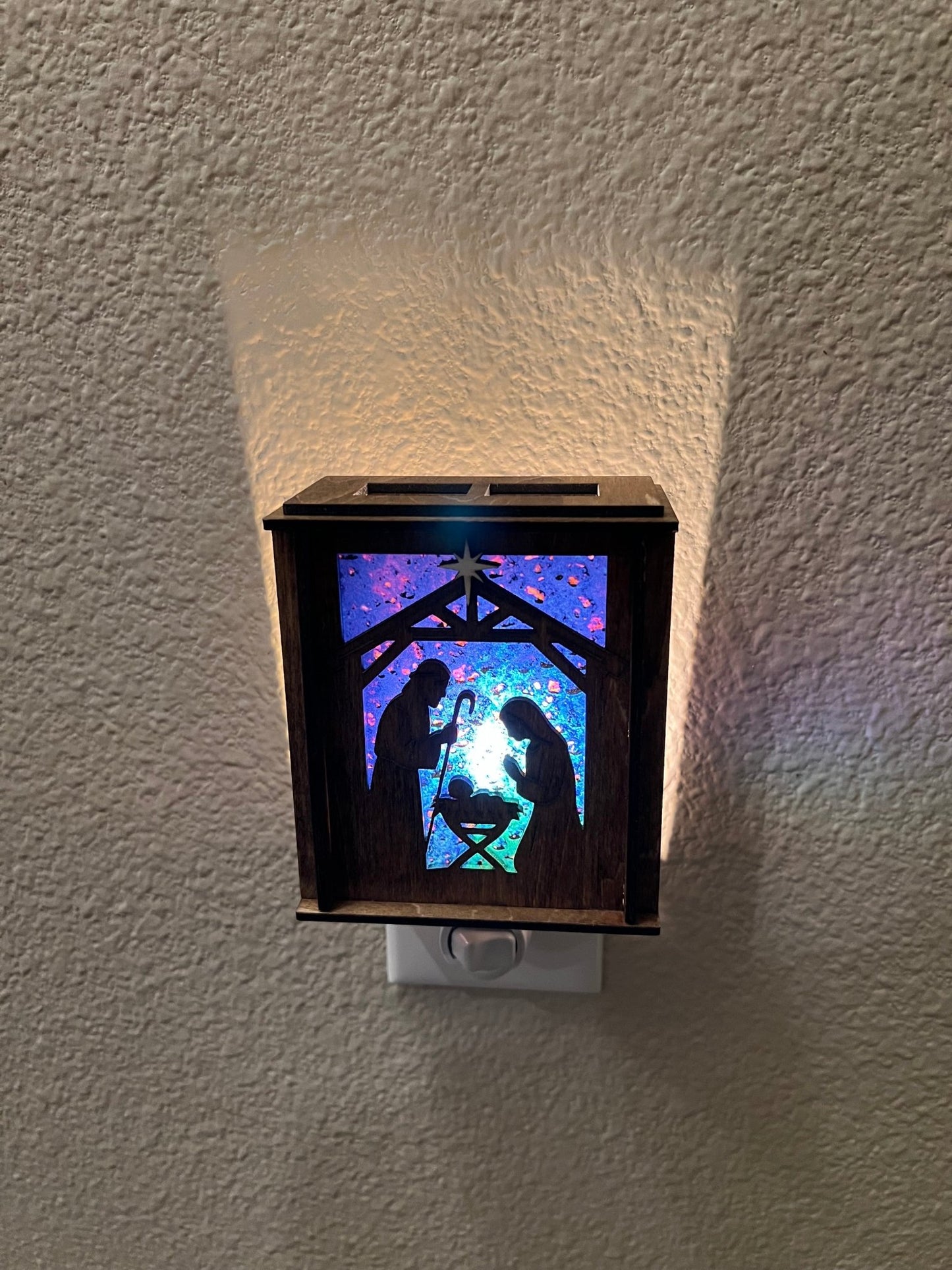 Golden oak stained wooden and acrylic nativity nightlight with rustic charm front view plugged in and lit.