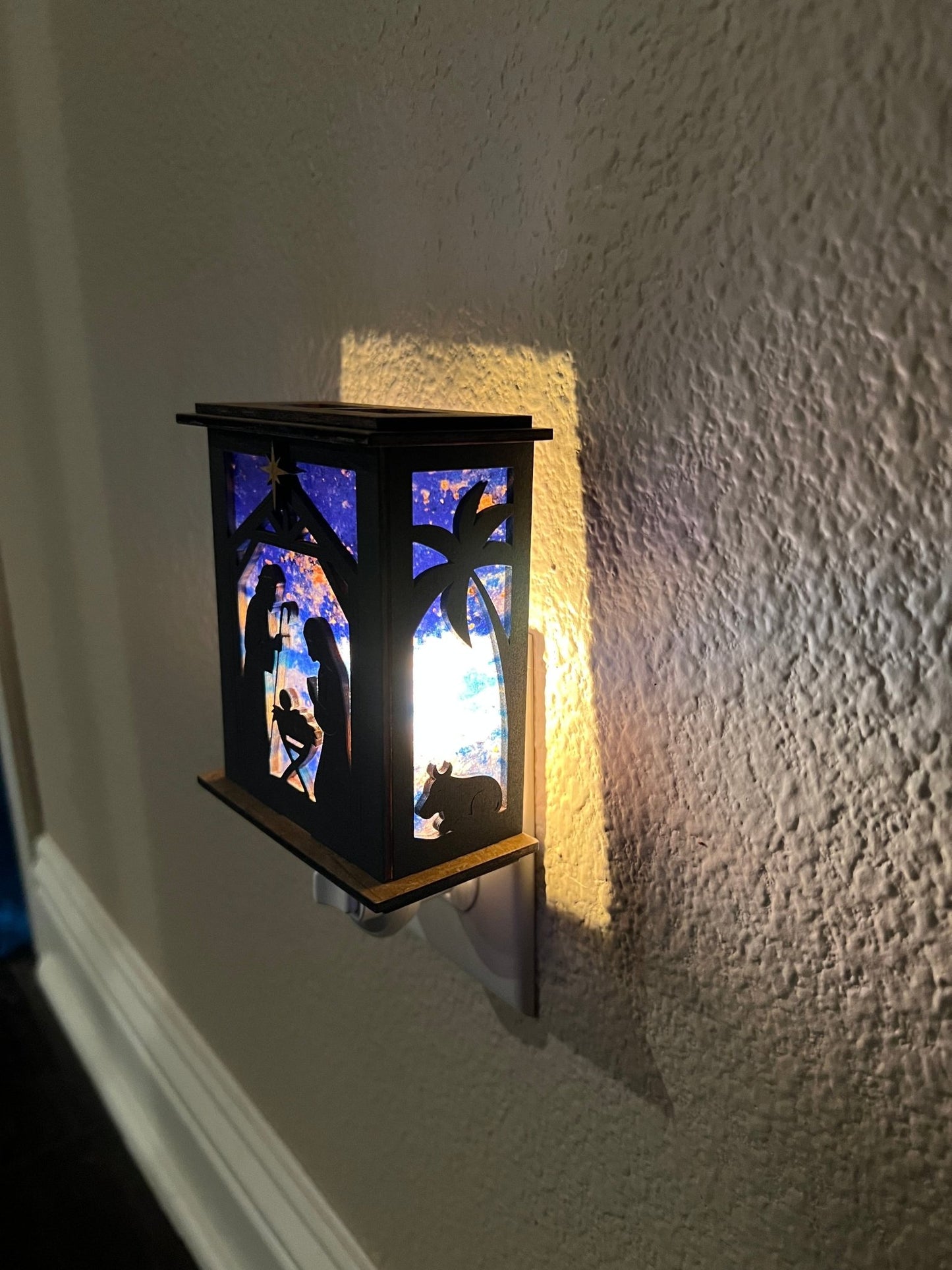 Rustic nativity nightlight lantern made of black wood and golden oak stained acrylic plugged in with right view and lit.